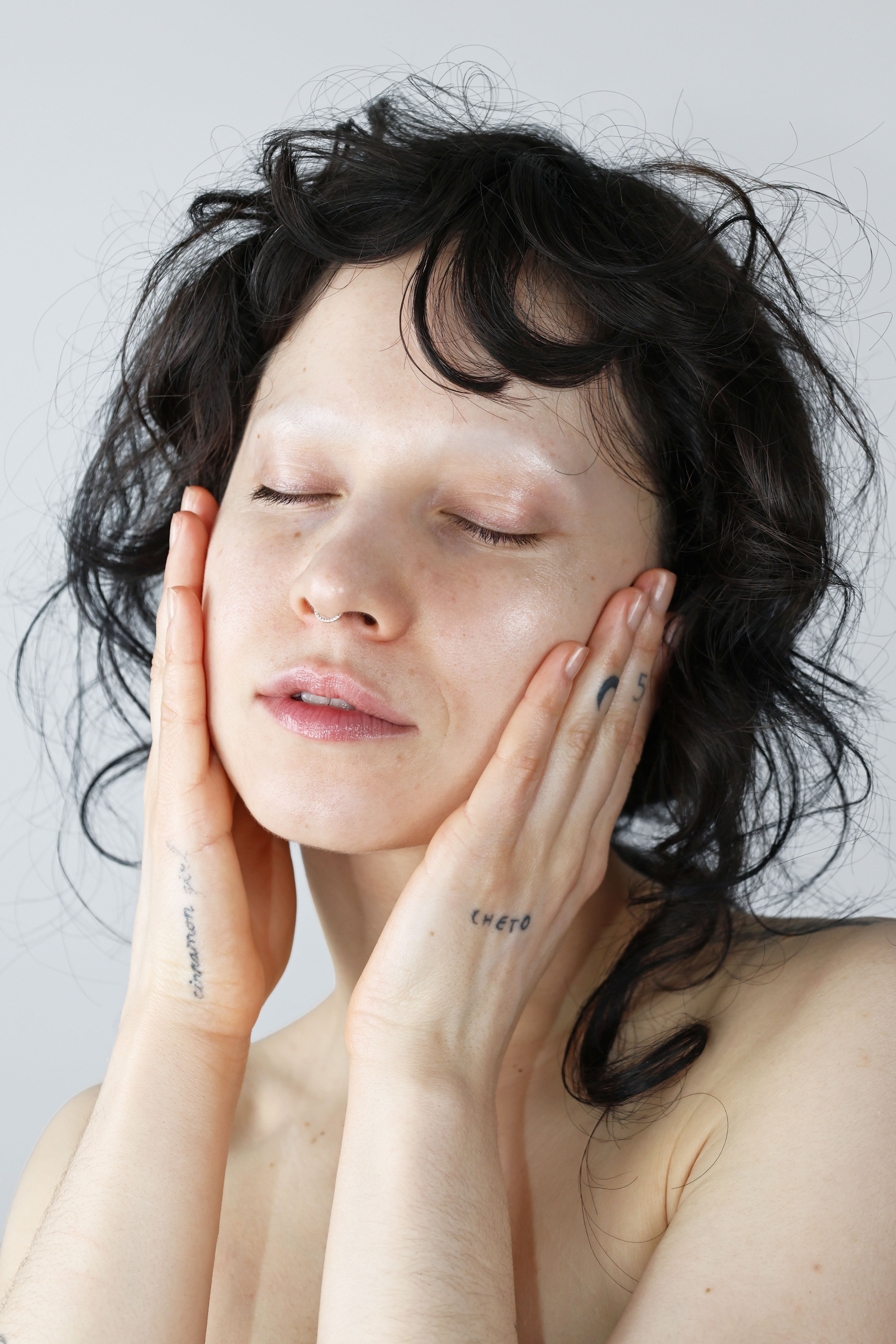 QUINTA skincare campaign — a person with glowing, moisturized skin pressing hands to their face, eyes closed in a moment of calm. Natural barrier repair skincare for sensitive and dry skin, hand-formulated in Berlin.