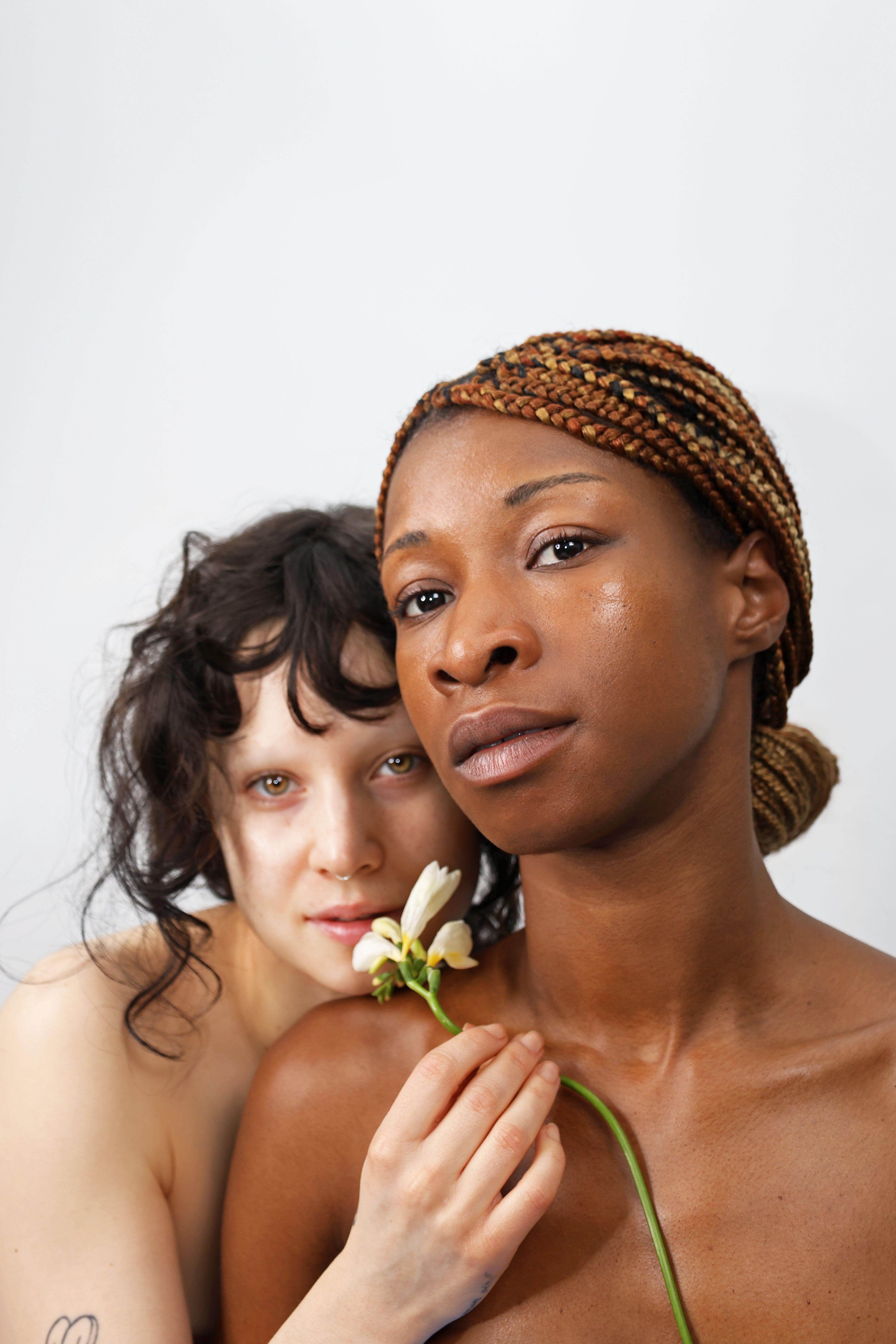 Two women embracing, one holding a flower, against a plain background