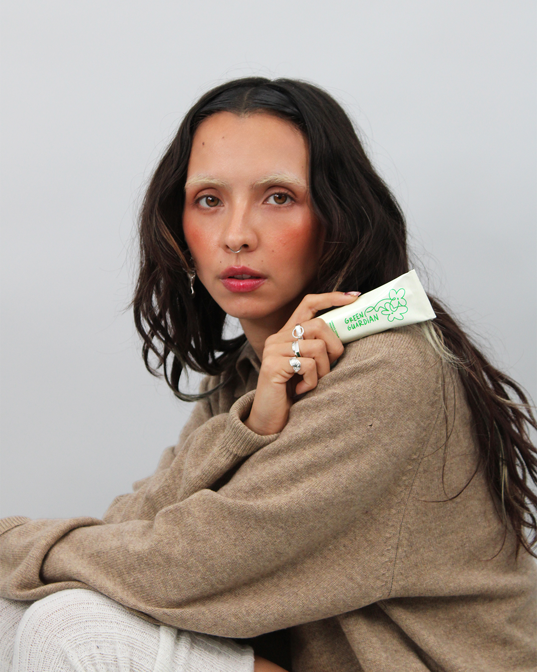 Woman in a cozy sweater holding a tube of Green Guardian Barrier Repair Moisturizer against a plain background
