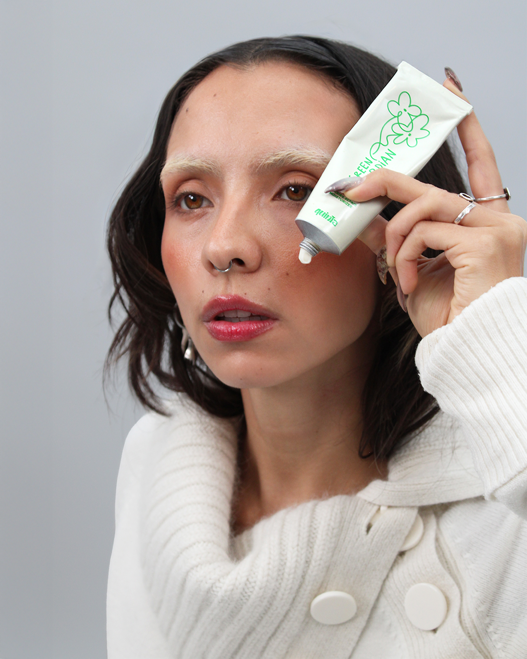 Woman applying a skincare product to her face with a gray background