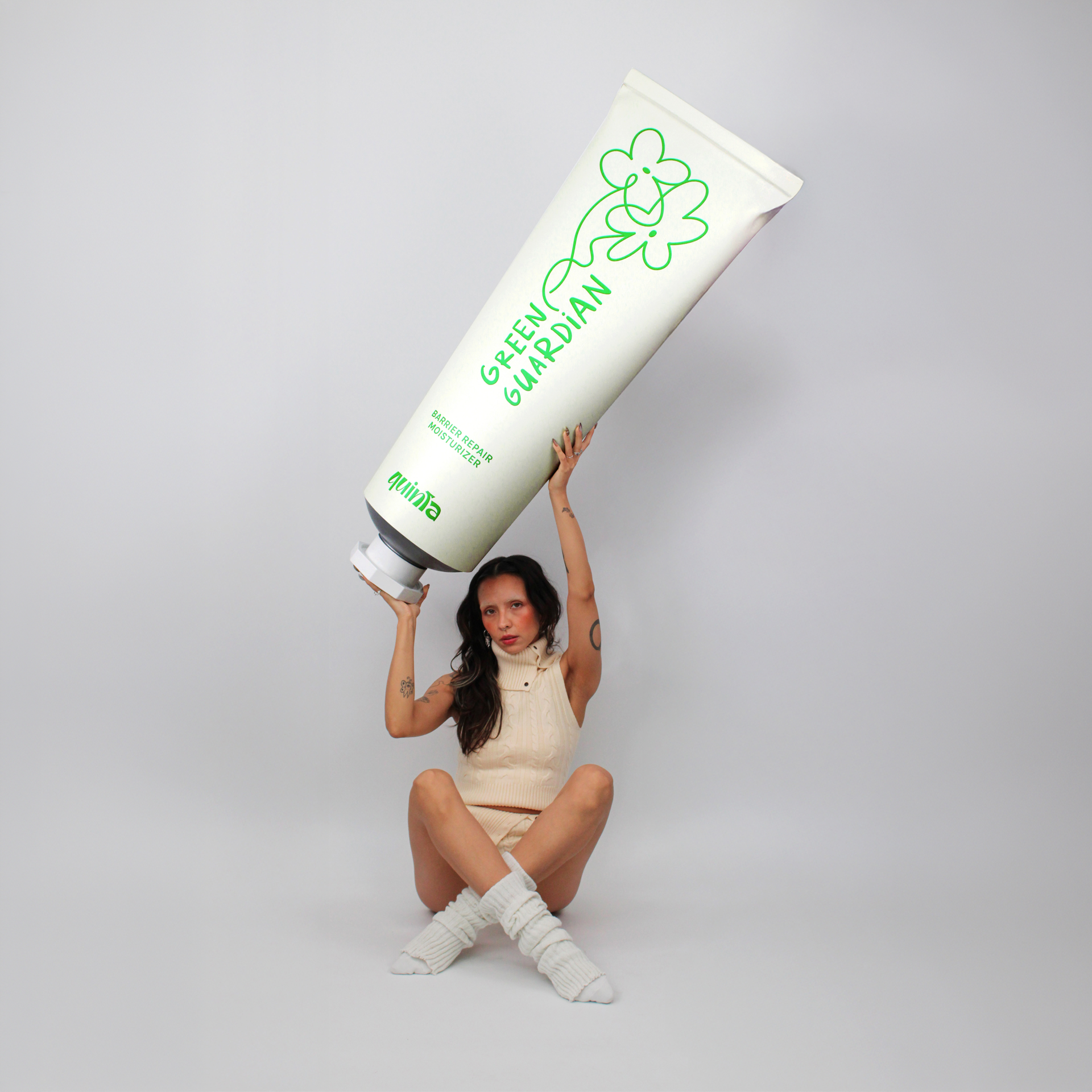 Person holding a large tube of 'Green Guardian' moisturizing cream against a gray background