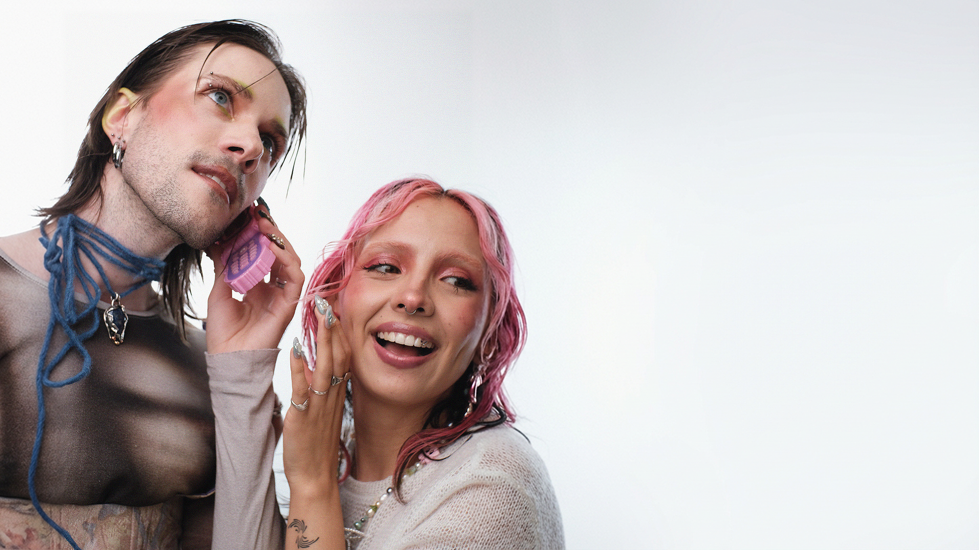 Two people with colorful hair on a white background talking to a flip phone