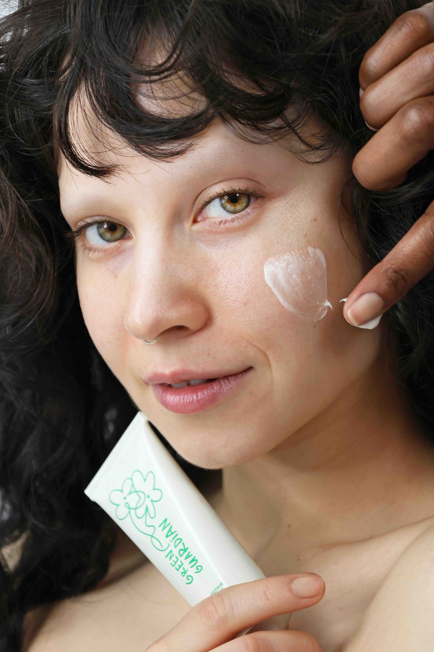 model applying quinta green guardian barrier repair moisturizer to cheek with tube in hand