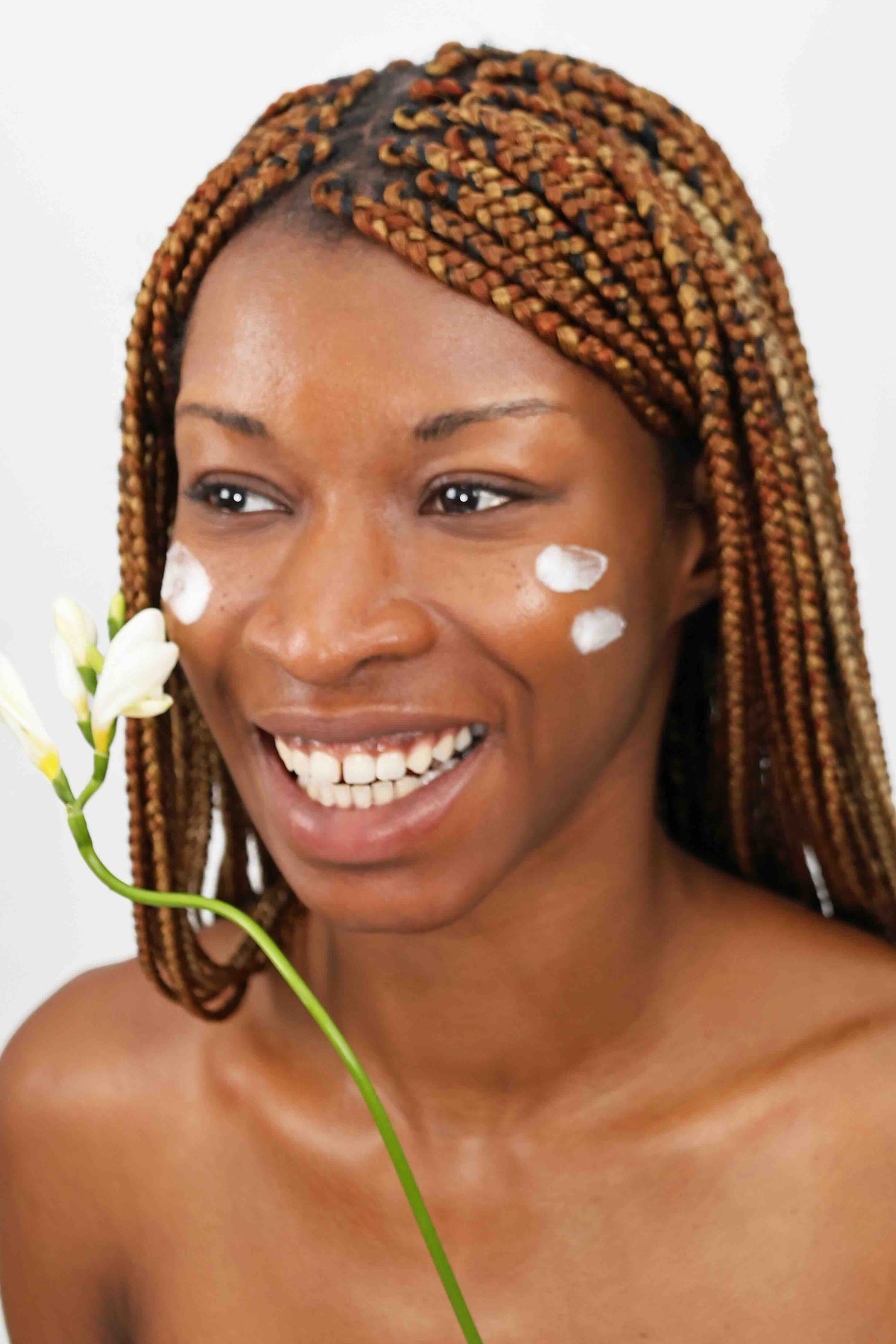 smiling model with cream applied to cheeks holding flower for quinta green guardian natural skincare campaign