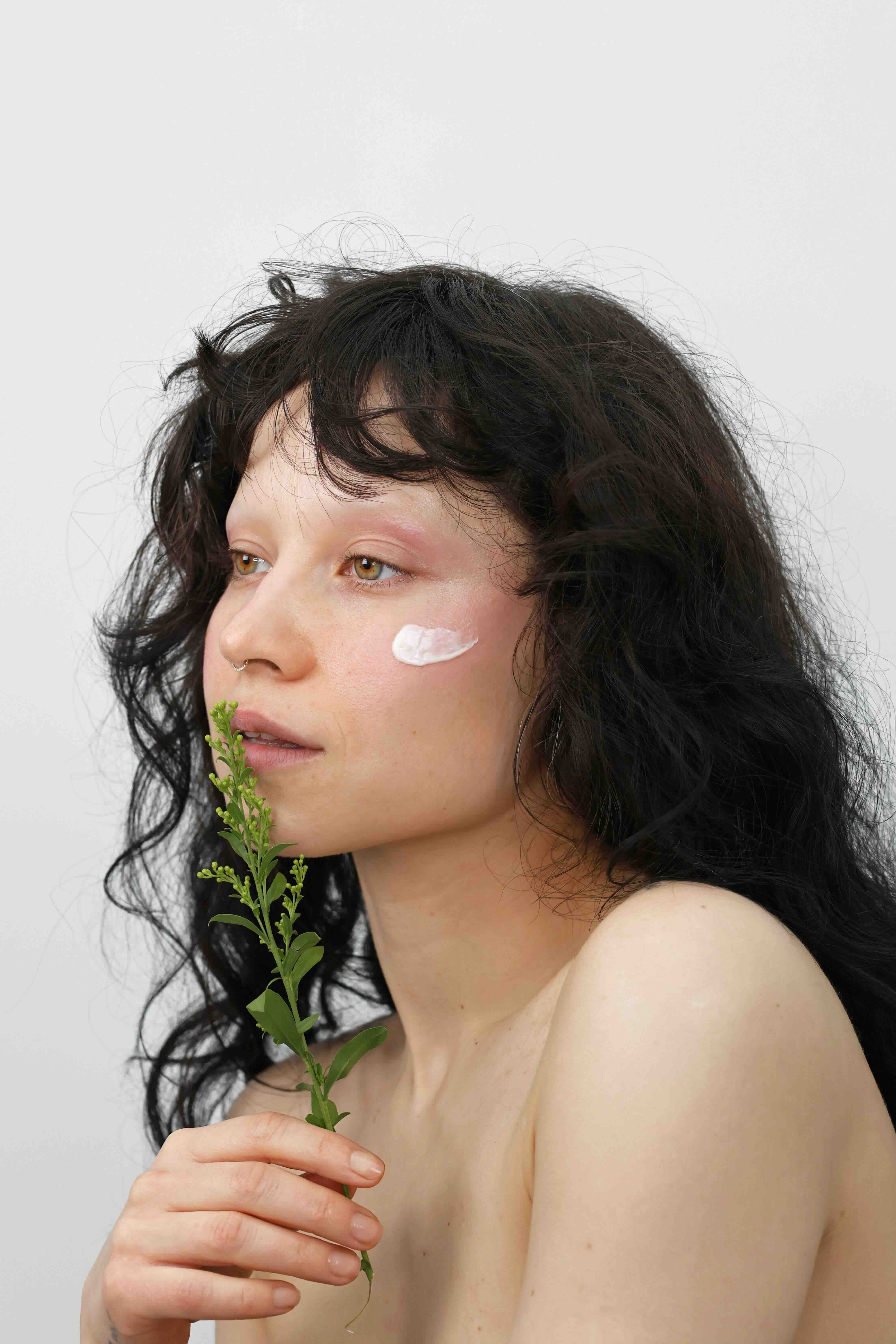 model with cream applied to cheek holding green botanical for quinta natural skincare campaign