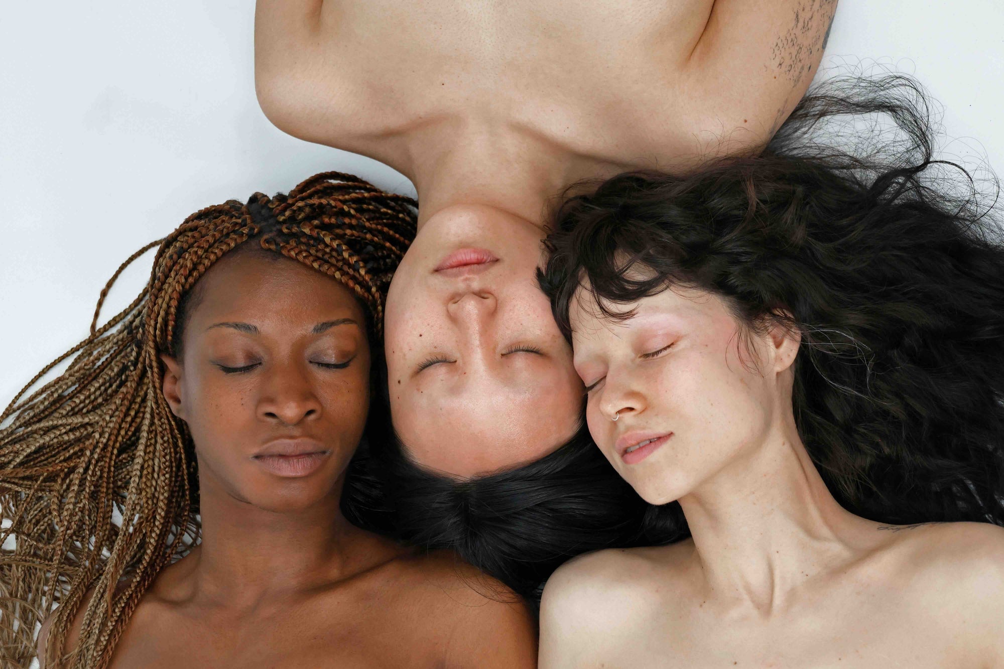three women with different skin tones lying together eyes closed for quinta real skin campaign