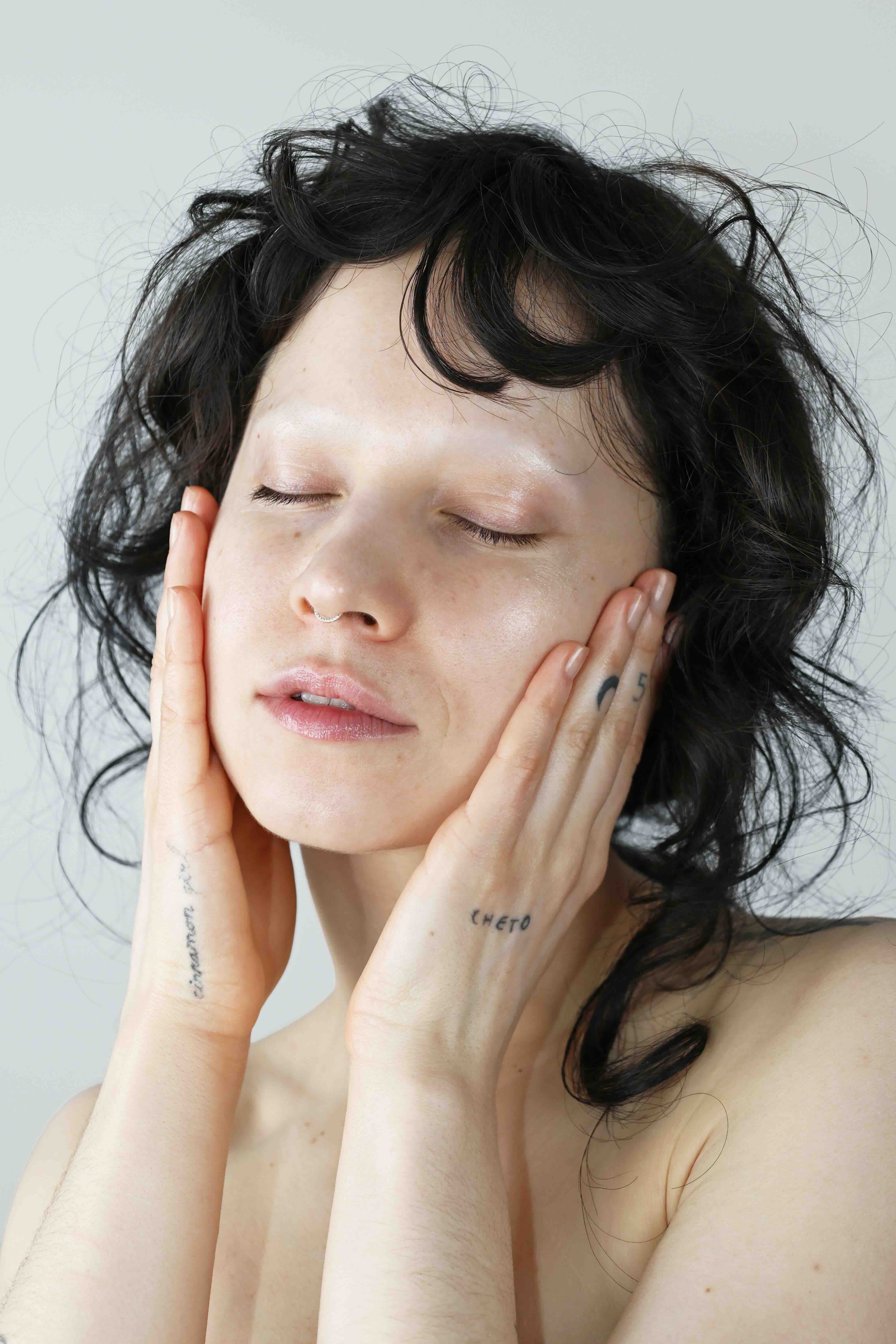 model with tattoos and nose ring holding face eyes closed for quinta sensitive skin barrier repair campaign