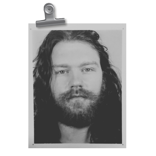 Black and white photo of Taylor, Co-Founder of Quinta, with long hair and beard on a clipboard.